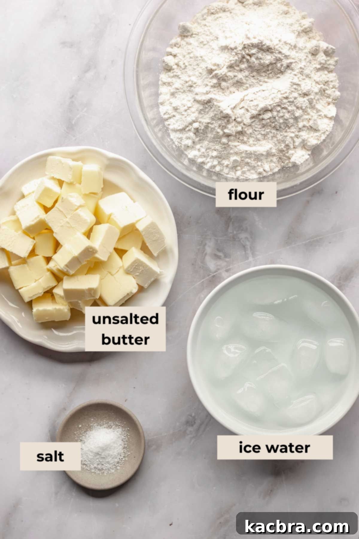 A beautifully arranged selection of fresh, high-quality ingredients for all-butter pie crust, including flour, cold butter, salt, and a glass of ice water.