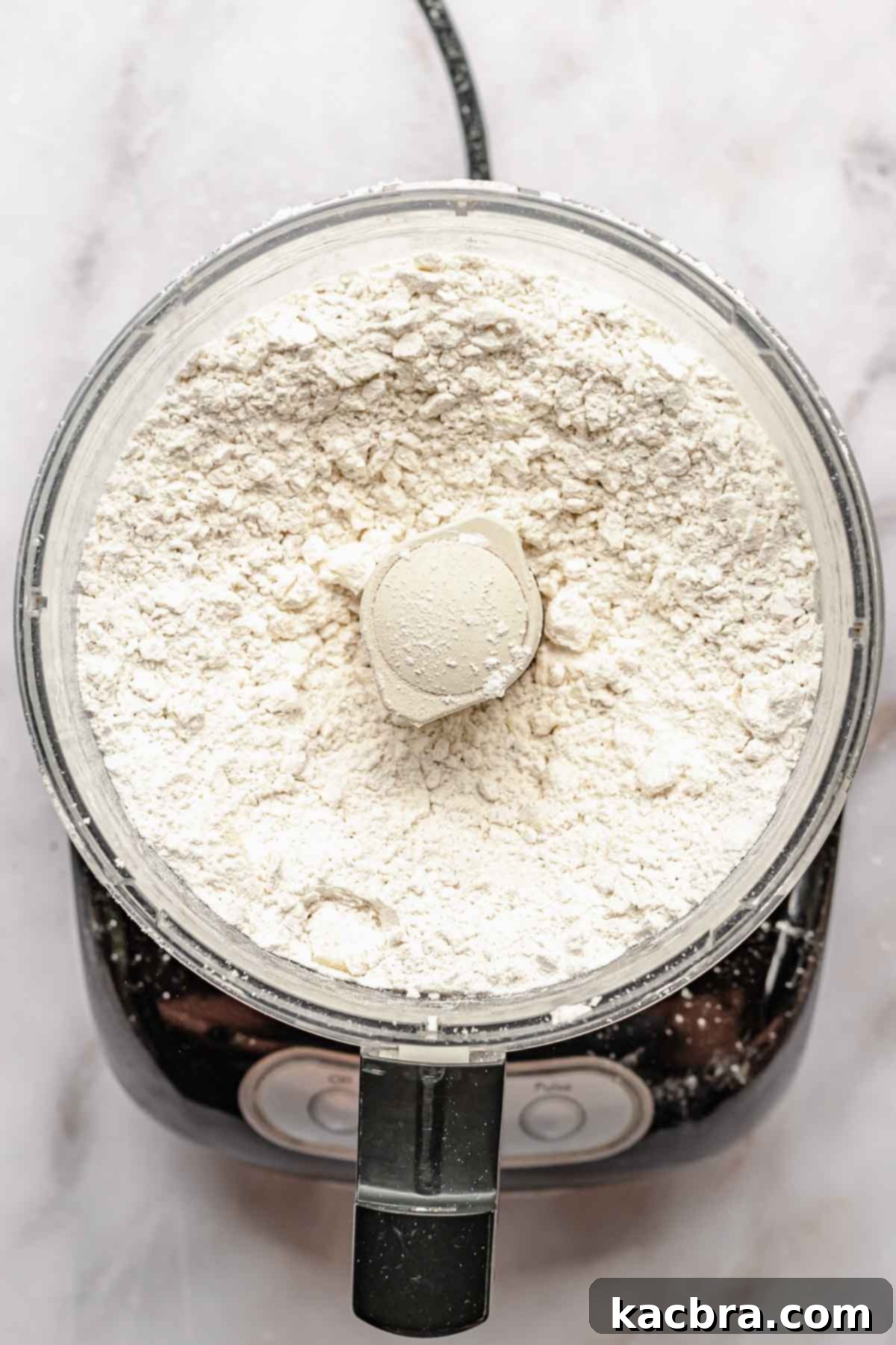 A close-up shot of blended butter and flour in a food processor, showing pea-sized butter pieces mixed throughout the flour.