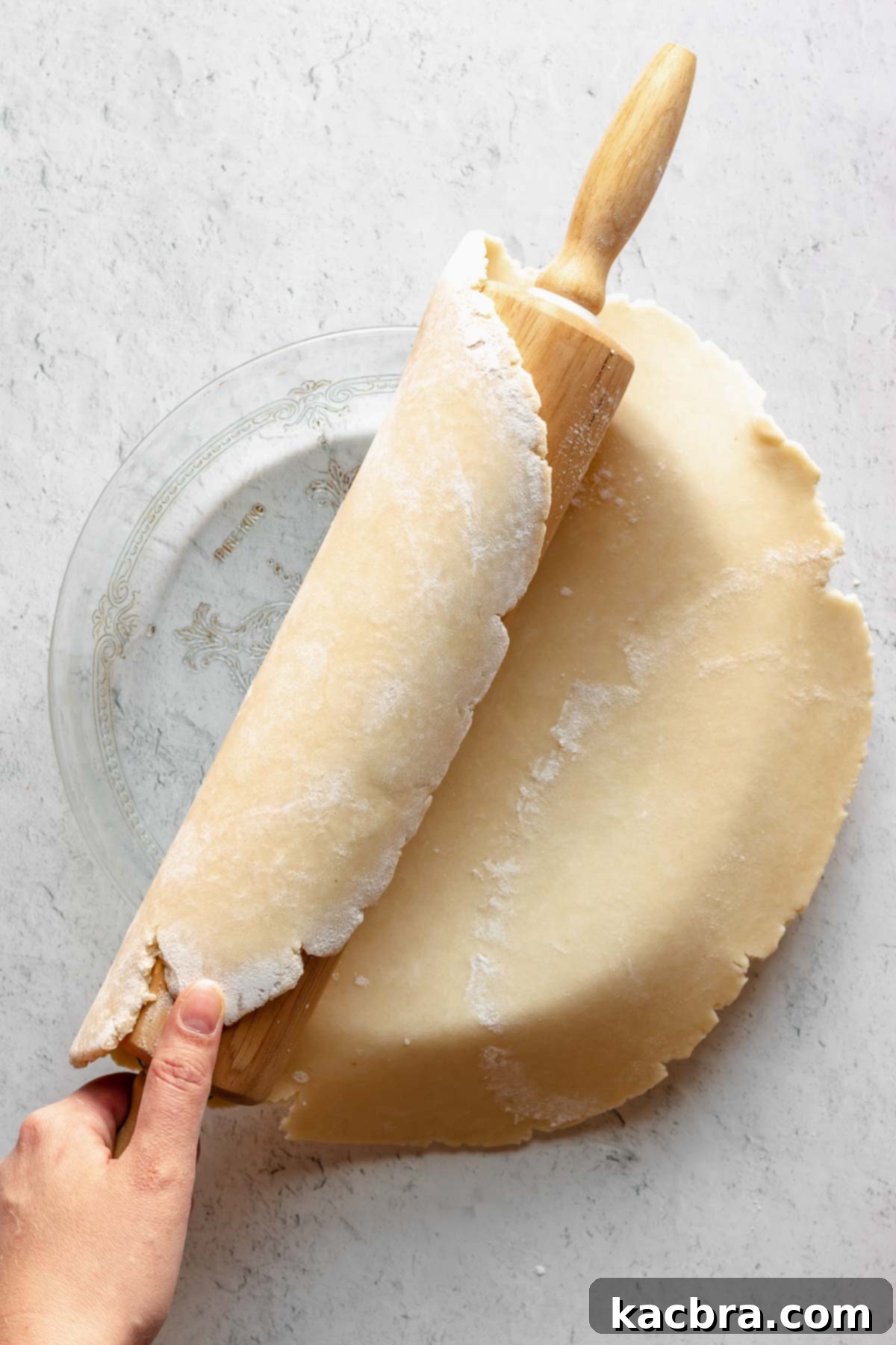 A freshly rolled pie dough gently being placed into a pie dish, showing the initial fit and overhang.