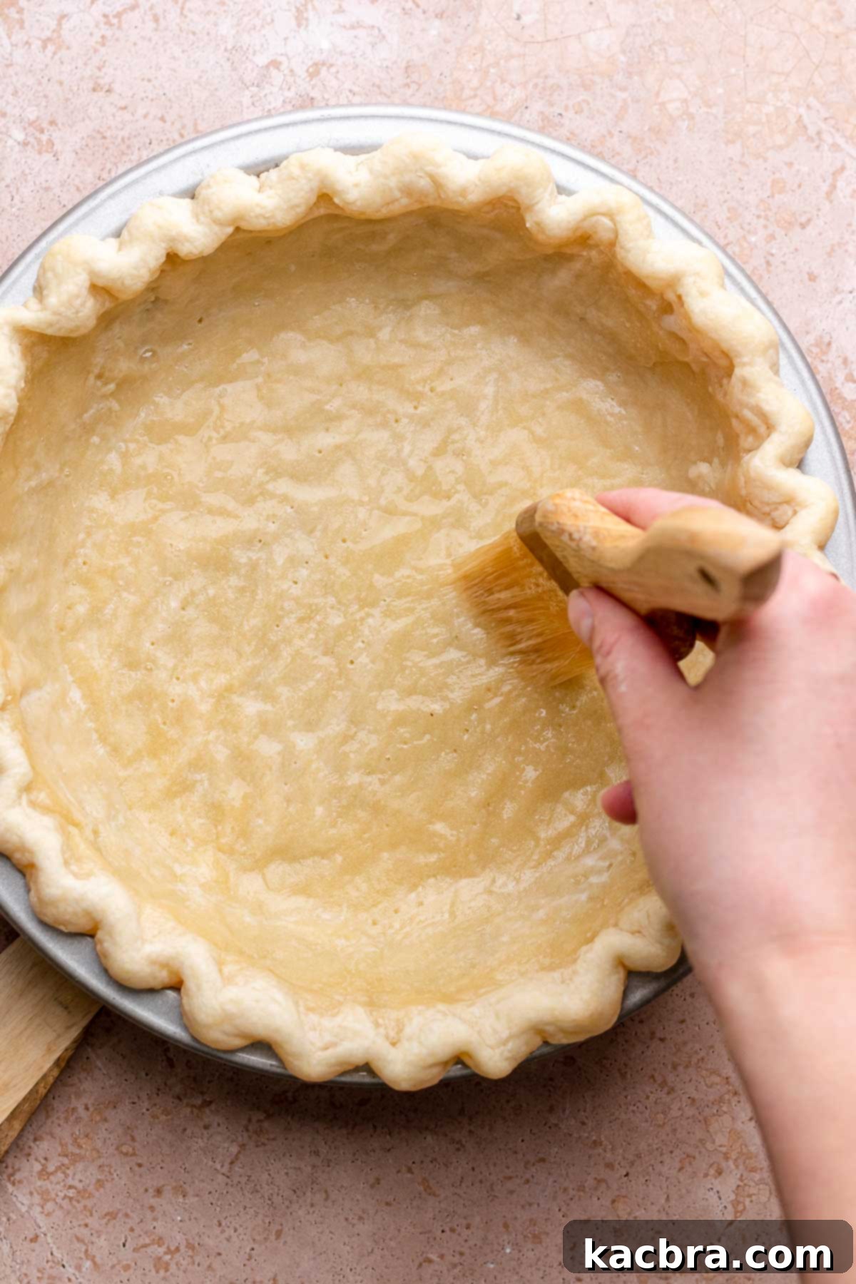 A pastry brush applies egg white wash to a par-baked pie crust.