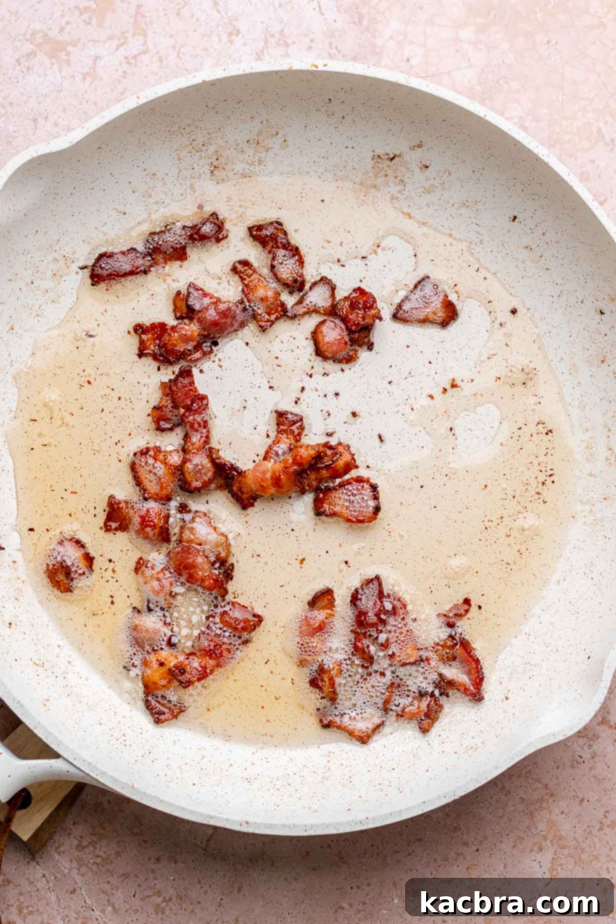 Crispy bacon pieces cooking in a pan.