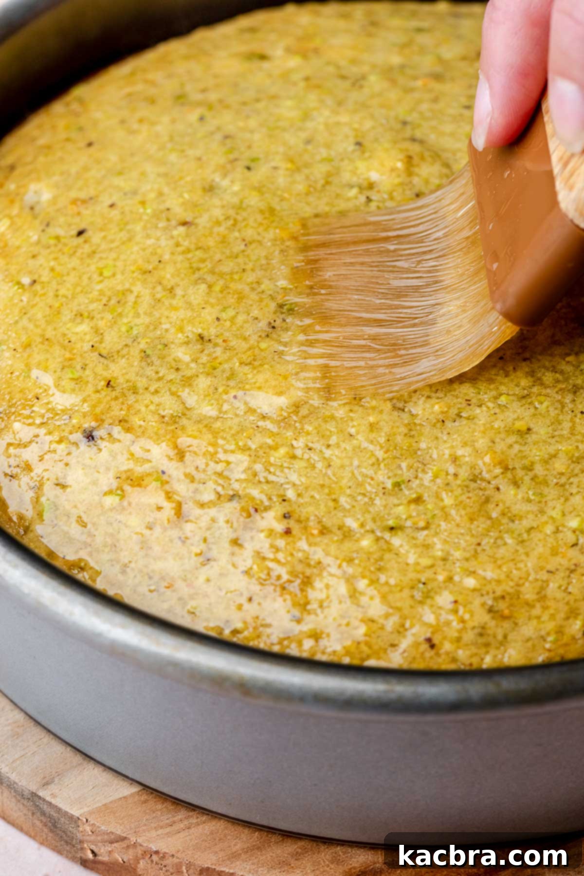 Golden Lemon Pistachio Dream with Honey Mascarpone Cloud 12 A pastry brush applying warm lemon syrup to the top of a freshly baked pistachio cake, ensuring even absorption.
