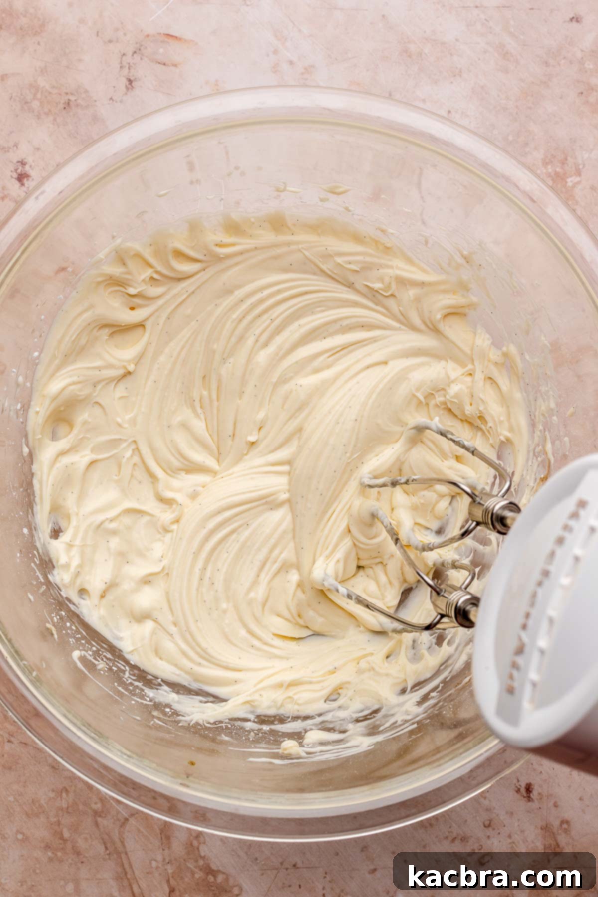 Golden Lemon Pistachio Dream with Honey Mascarpone Cloud 13 A hand mixer whipping honey lemon mascarpone frosting in a glass bowl, creating a light and creamy consistency.