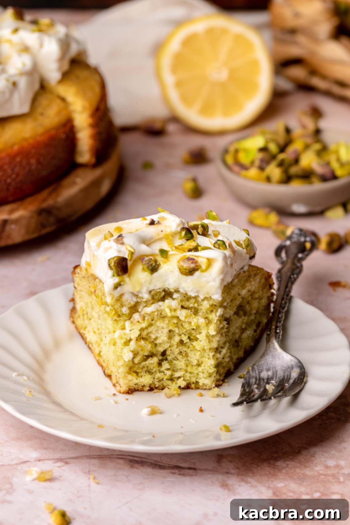 Golden Lemon Pistachio Dream with Honey Mascarpone Cloud 16 A perfect slice of lemon pistachio cake on a white plate, with a fork having taken a bite, showcasing its moist interior.