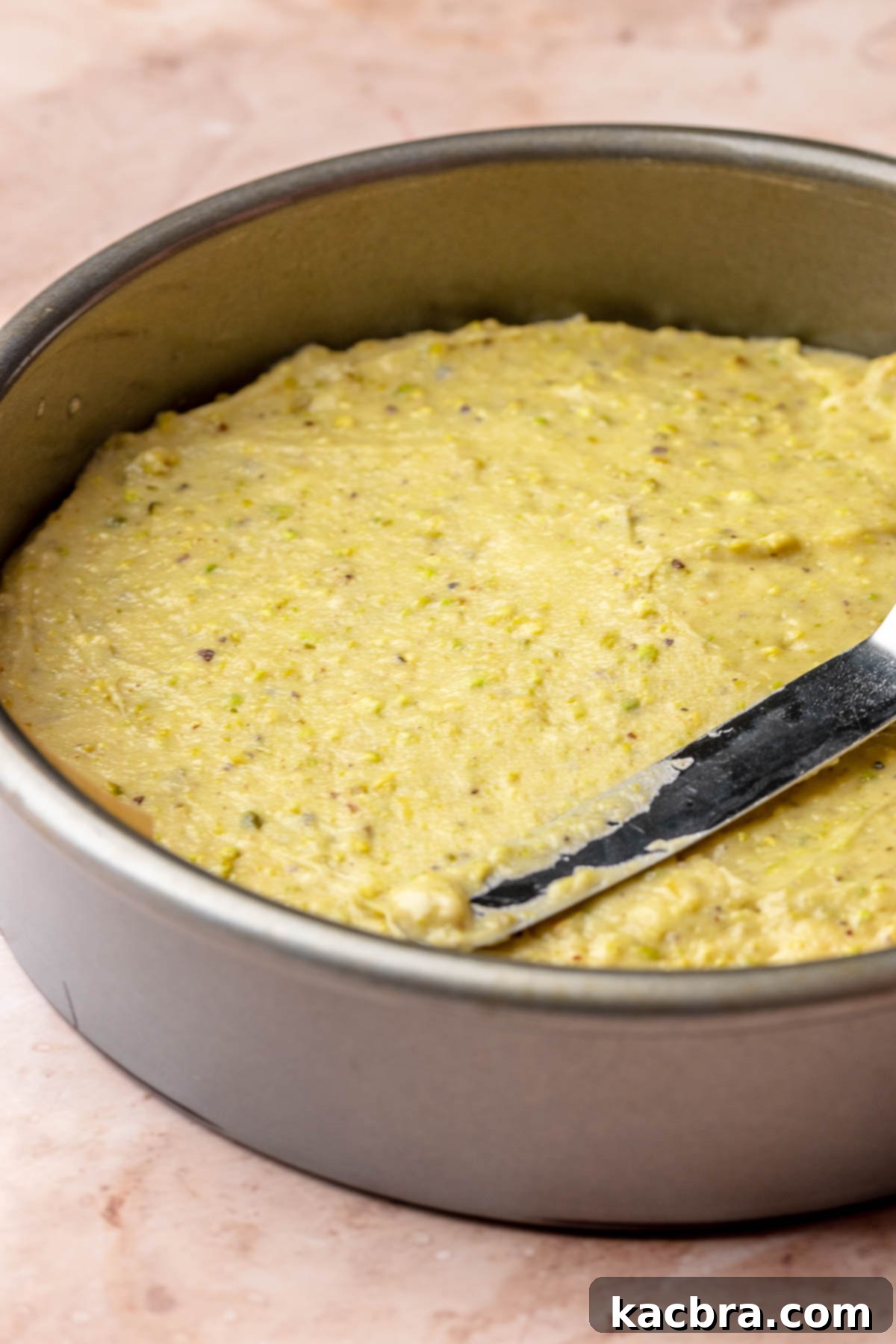 Golden Lemon Pistachio Dream with Honey Mascarpone Cloud 10 A spatula spreading the lemon pistachio cake batter evenly into a prepared 8-inch round baking pan.