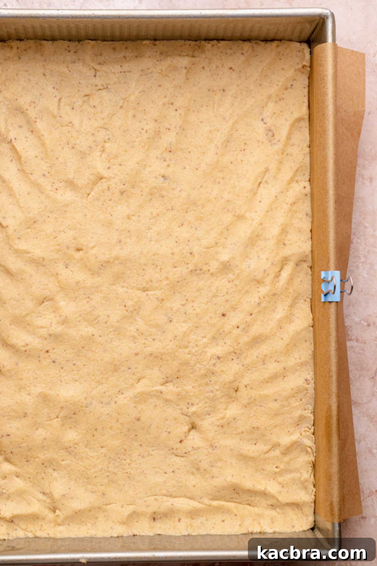 A layer of shortbread dough expertly pressed into a parchment-lined baking pan, ready for par-baking.