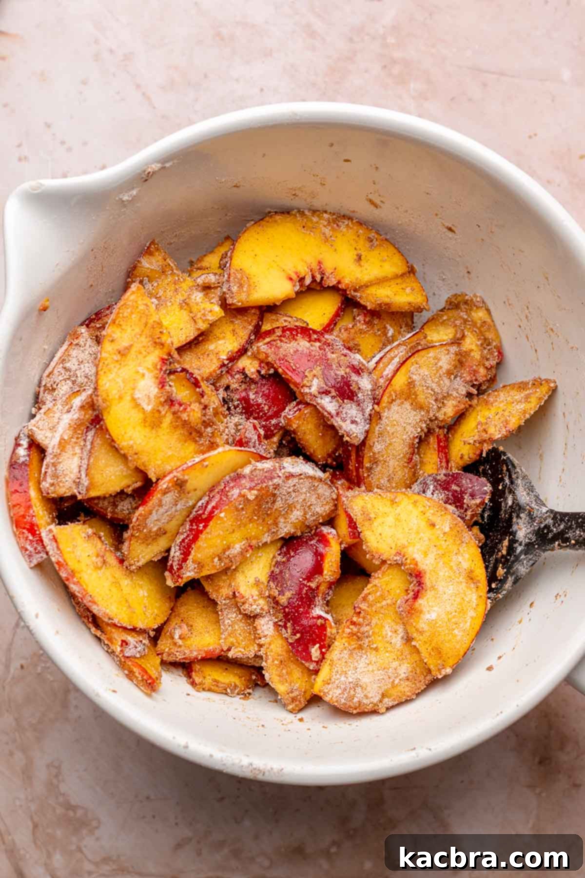 Freshly sliced peaches mixed with flour and a blend of warm spices in a bowl, ready for layering.