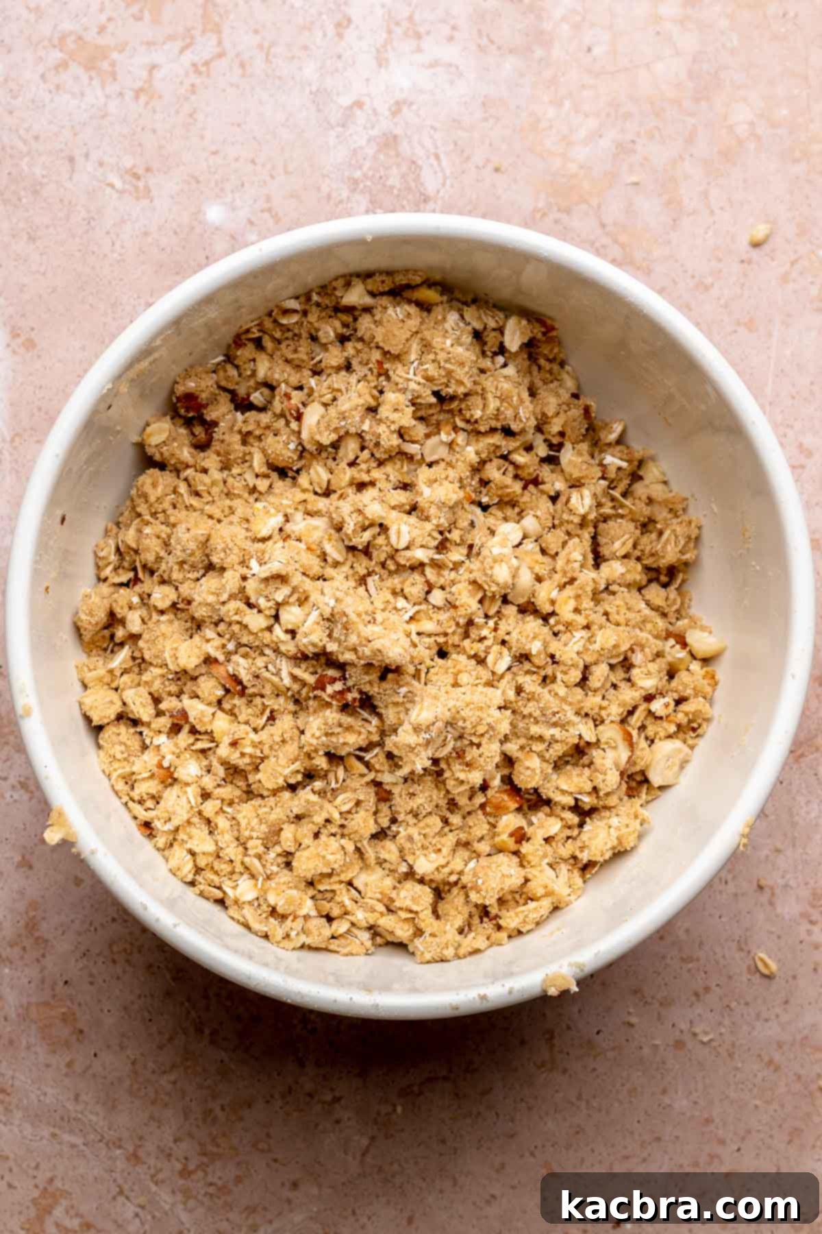 A bowl filled with the crumble topping mixture, featuring oats, flour, brown sugar, butter, and chopped hazelnuts, ready to be sprinkled.