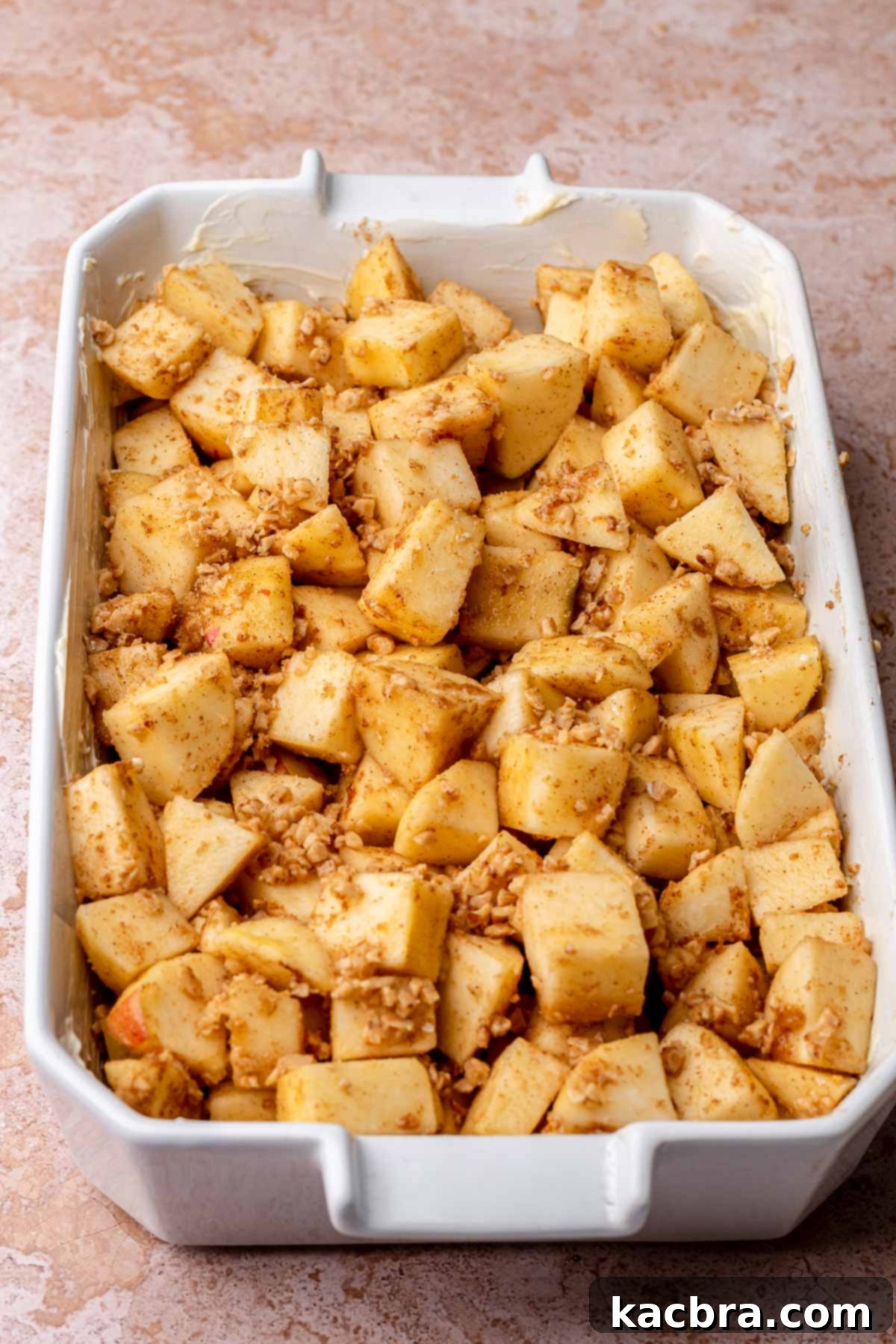 Cinnamon-spiced apple filling spread evenly in a buttered casserole dish, awaiting the crumble topping.