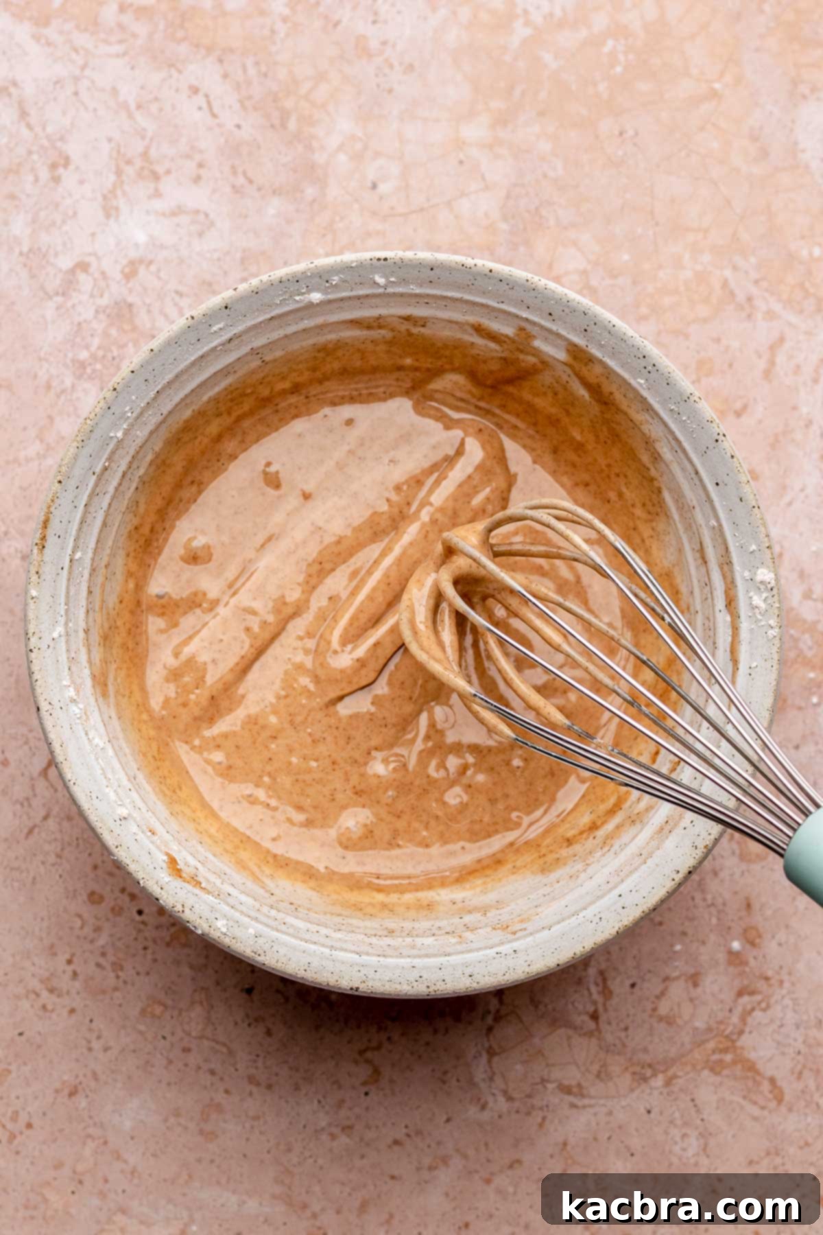 A bowl of freshly prepared cinnamon glaze with a whisk, showing its smooth consistency.