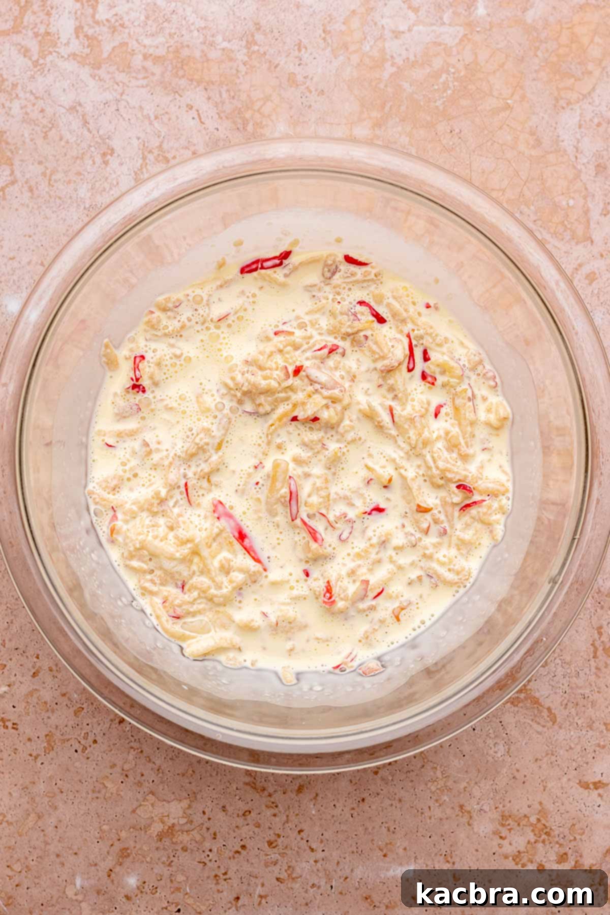 A bowl containing whisked eggs, heavy cream, and grated apples, mixed together.