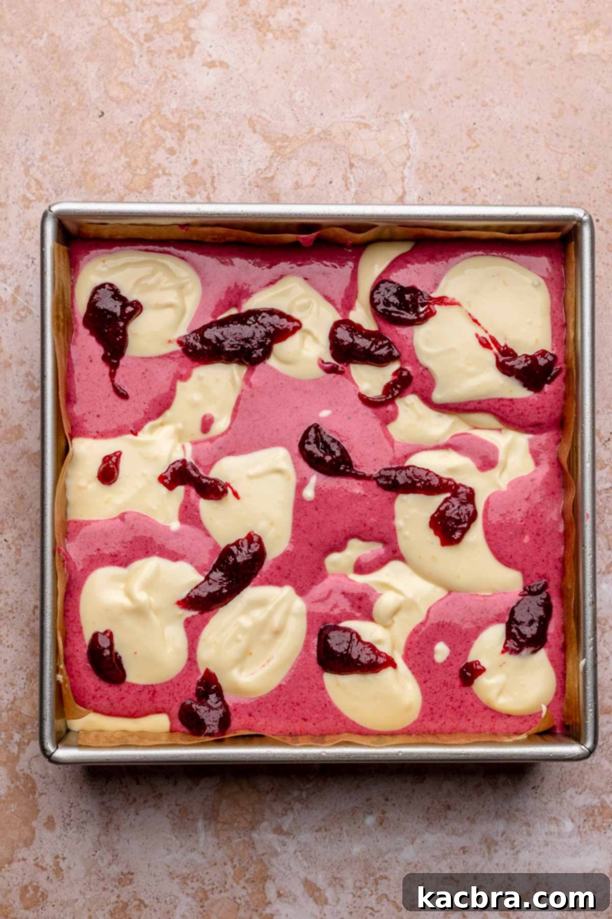 Alternating spoonfuls of cranberry and vanilla cheesecake batters are carefully placed on top of the baked gingersnap crust in a square pan.