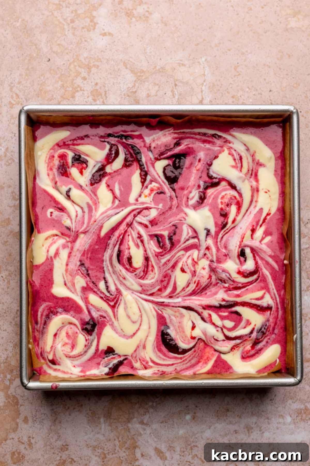 A butter knife is used to gently swirl the alternating cranberry and vanilla batters in the square pan, creating a beautiful marbled effect.