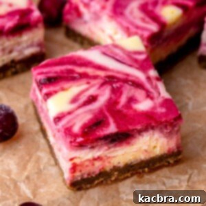 A square of a perfectly cut cranberry cheesecake bar, showcasing its layers and vibrant swirl, resting on parchment paper.