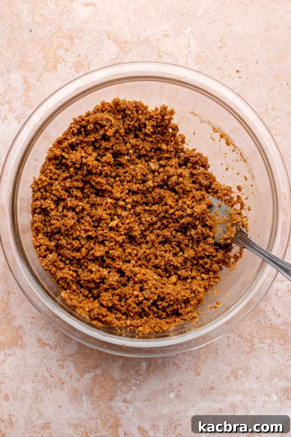 Finely ground gingersnap cookie crumbs, melted butter, and a pinch of salt are mixed in a bowl with a fork, ready for the crust.