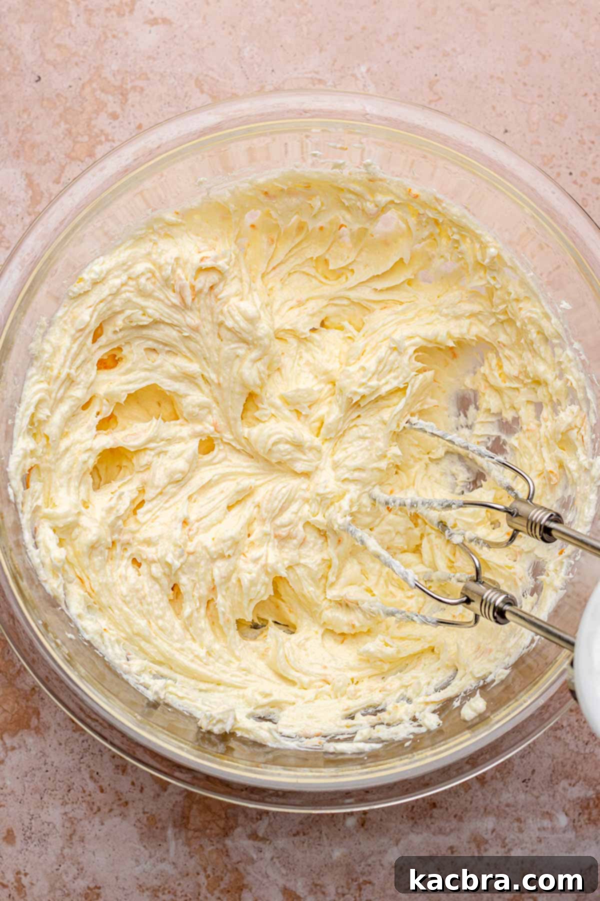 A hand mixer creaming softened cream cheese in a mixing bowl, ensuring a smooth, lump-free base for the cheesecake batter.