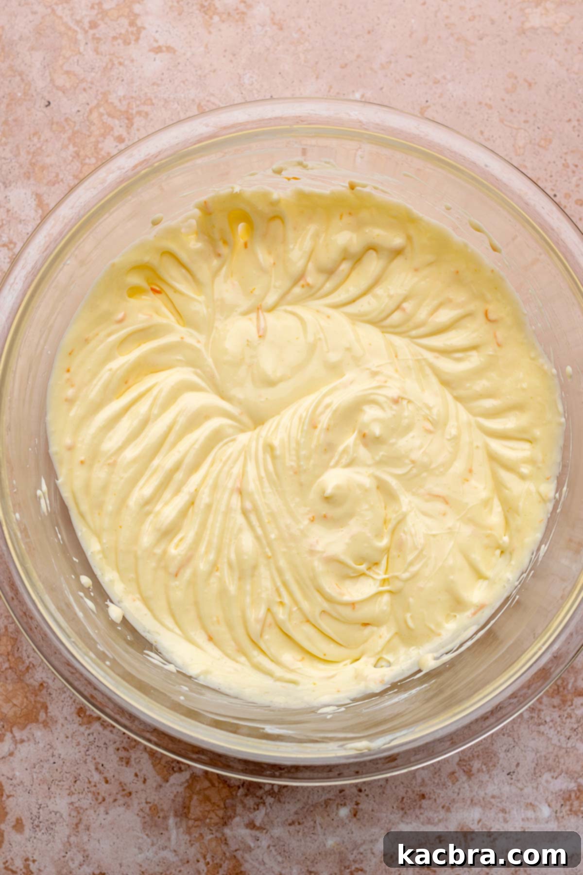 Whisked eggs are gradually added to the cream cheese mixture in a bowl and gently beaten to combine for the cheesecake batter.