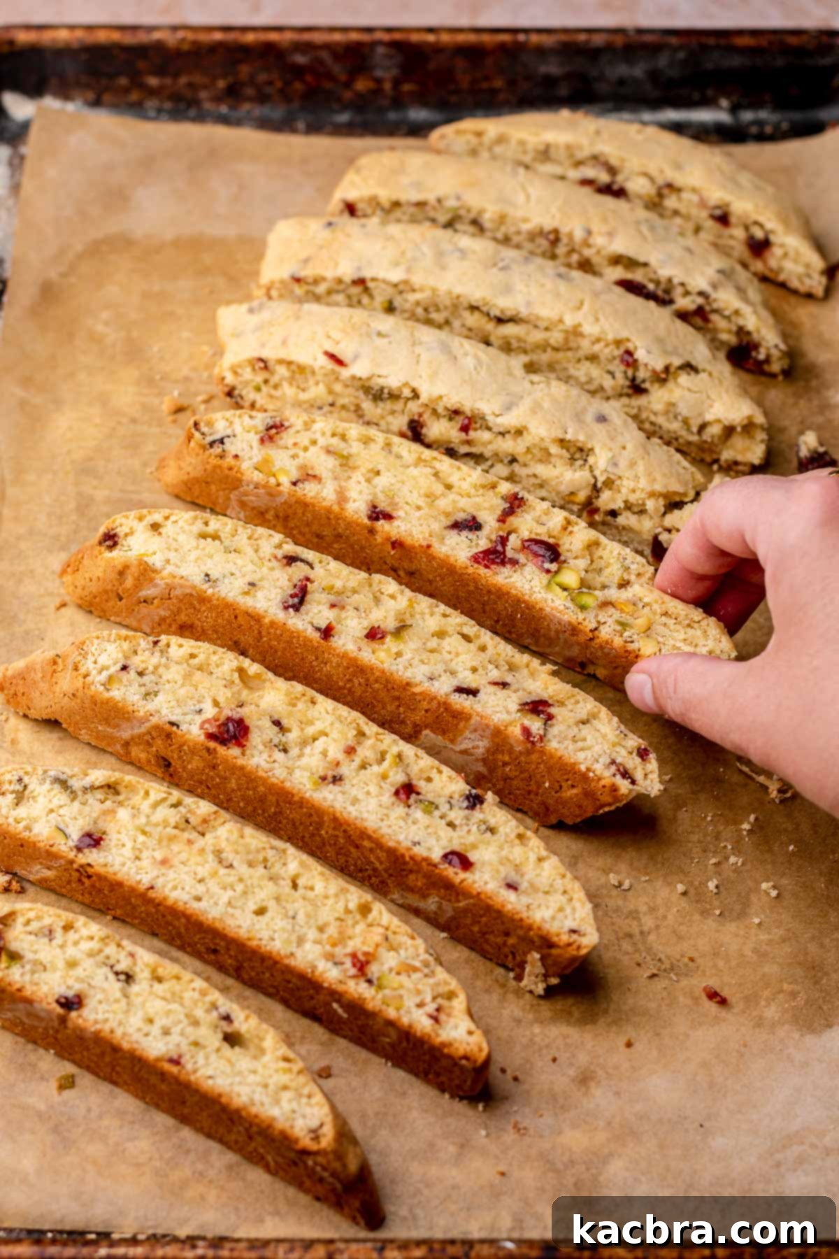 A hand arranging sliced biscotti pieces on their cut sides on a baking sheet, preparing them for the second bake.