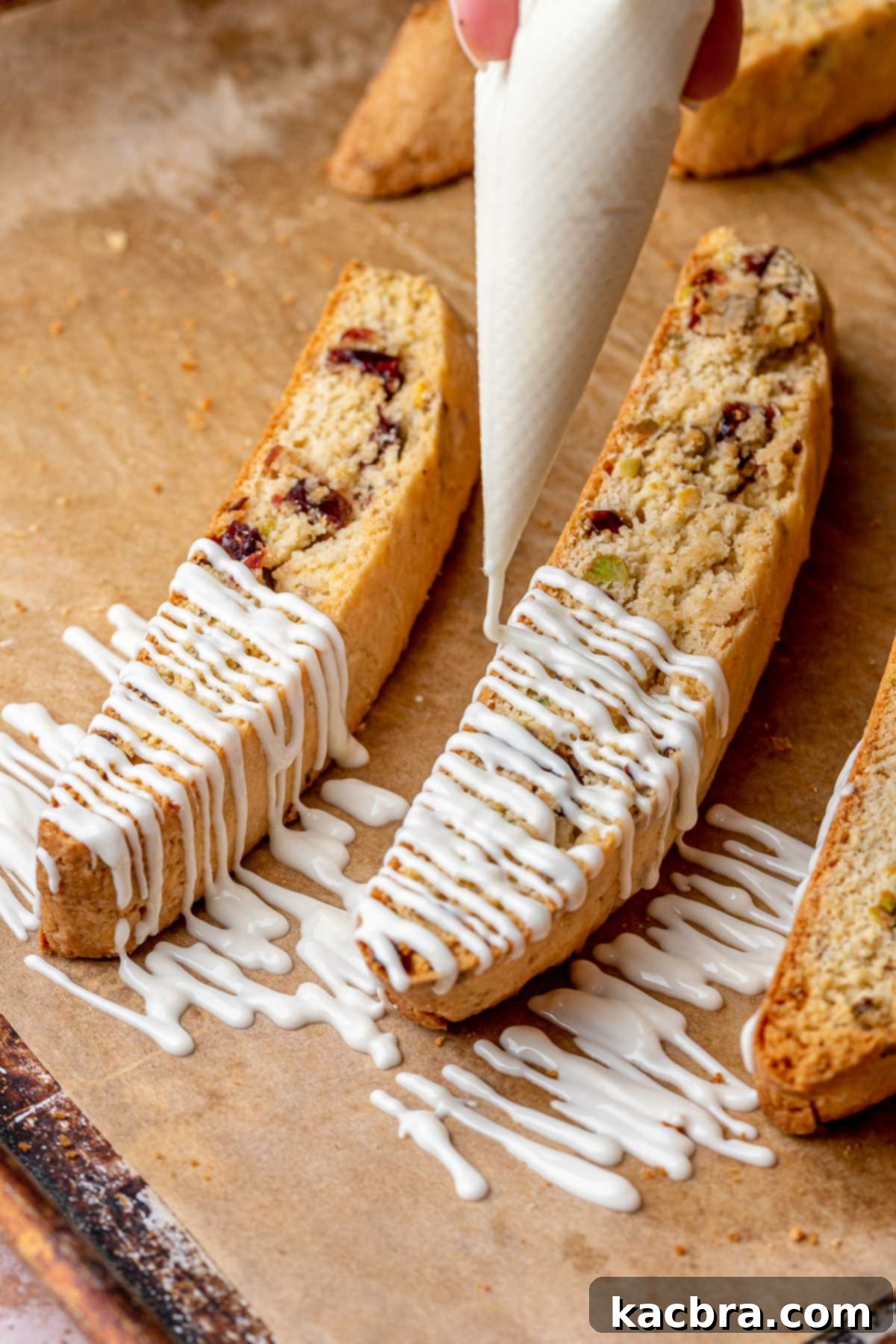 A piping bag elegantly drizzling melted white chocolate over freshly baked cranberry pistachio biscotti.