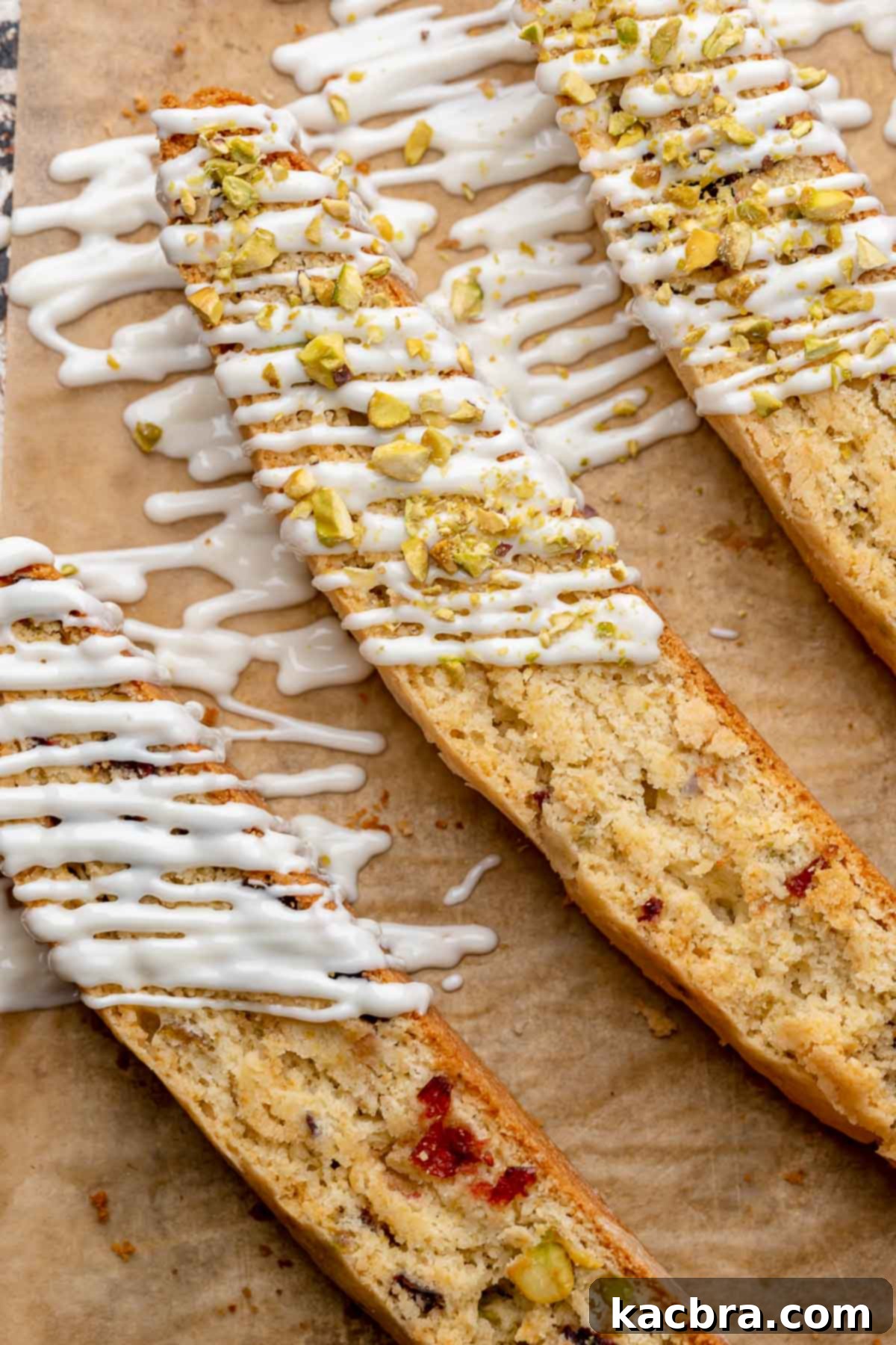 Three beautifully finished cranberry pistachio biscotti, adorned with a delicate white chocolate drizzle, presented on a plate.