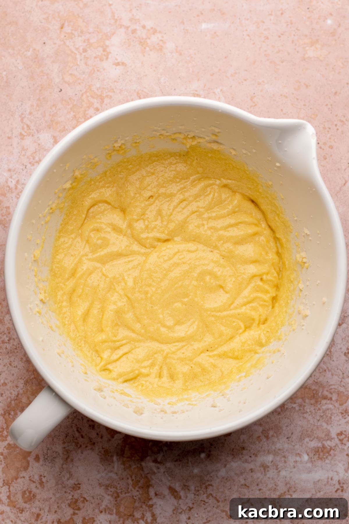 The creamed butter and sugar mixture, now with eggs incorporated, showing a smooth, well-emulsified texture.