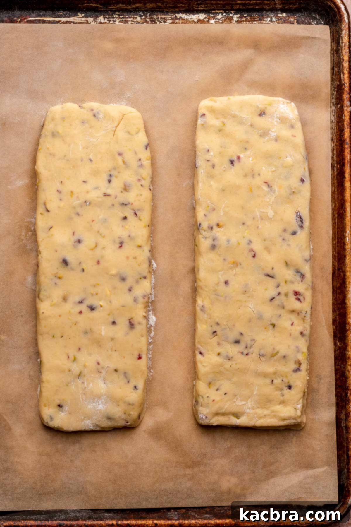 Two perfectly shaped logs of cranberry pistachio biscotti dough, ready for their first bake on a parchment-lined sheet pan.