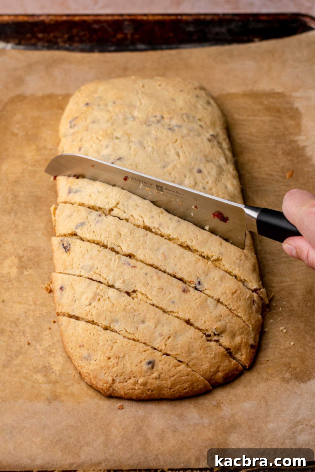 A knife cuts a mound of biscotti on the bias.