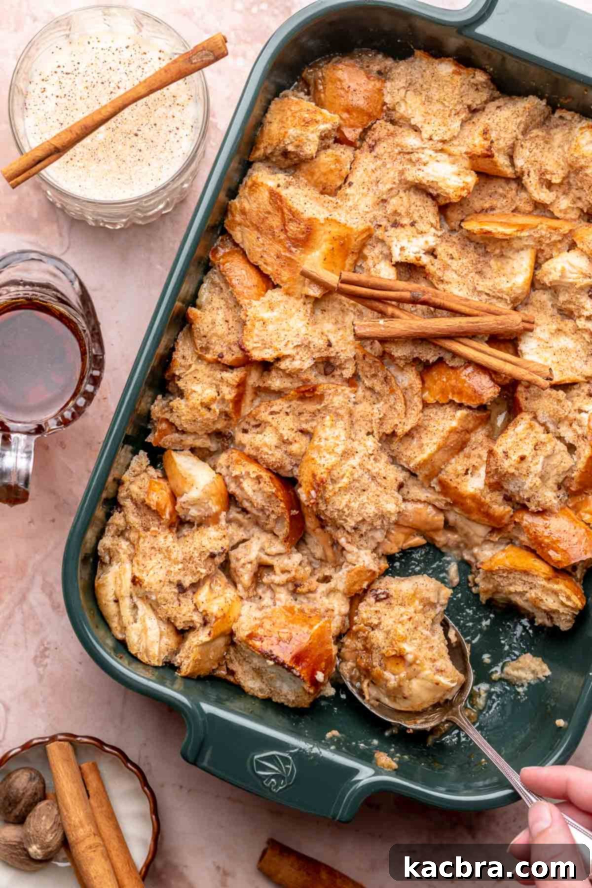 A hand scoops eggnog french toast casserole out of a dish, ready to serve, sixth step.