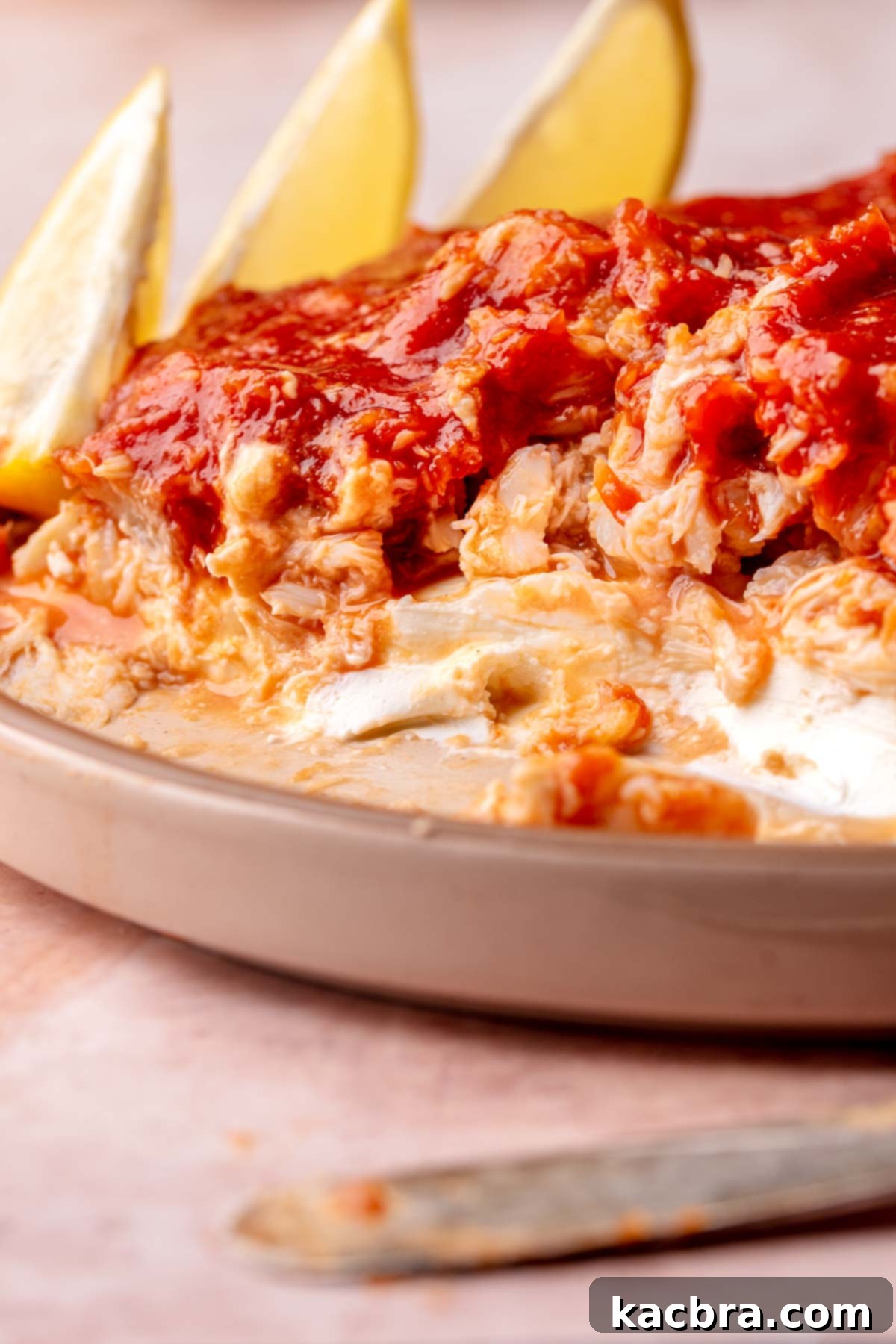 Half scooped cold crab dip on a plate showing visible layers of cream cheese, crab, and cocktail sauce.