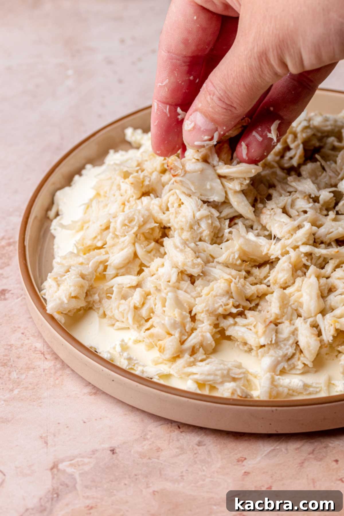 A hand gently adds lump crab meat on top of the cream cheese layer.