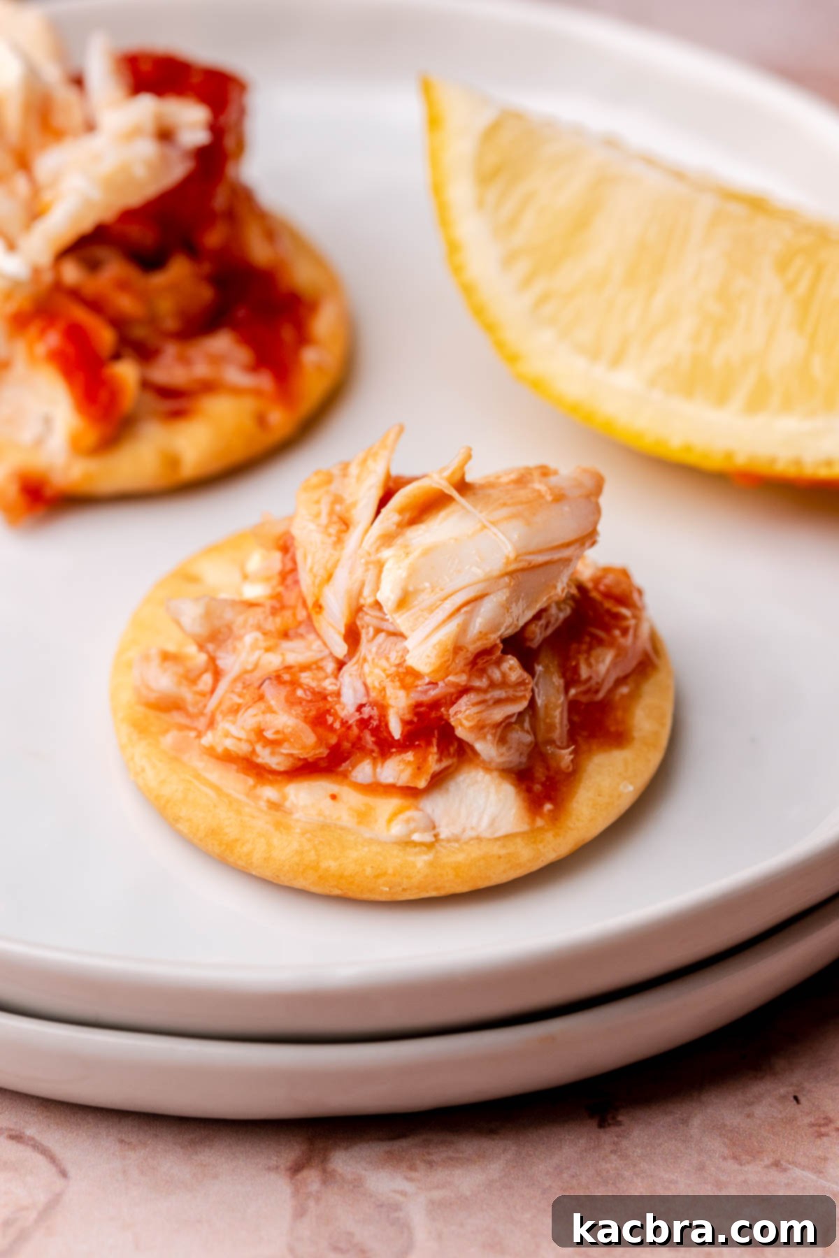 A cracker topped with cold crab dip, showing the three distinct layers, resting on a serving plate.