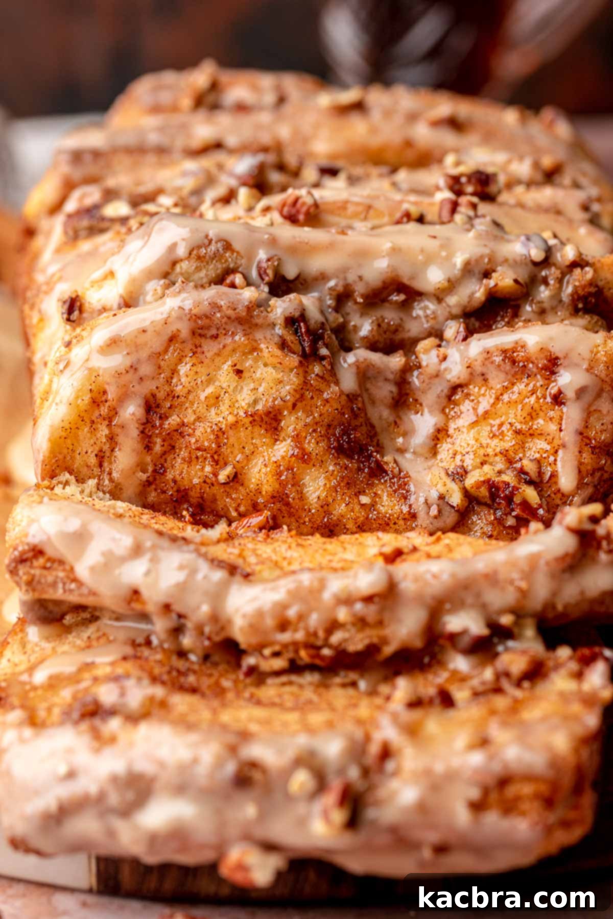 Golden brown maple pecan cinnamon pull apart bread on a wooden cutting board with two pieces gently pulled away, revealing its soft, layered interior.