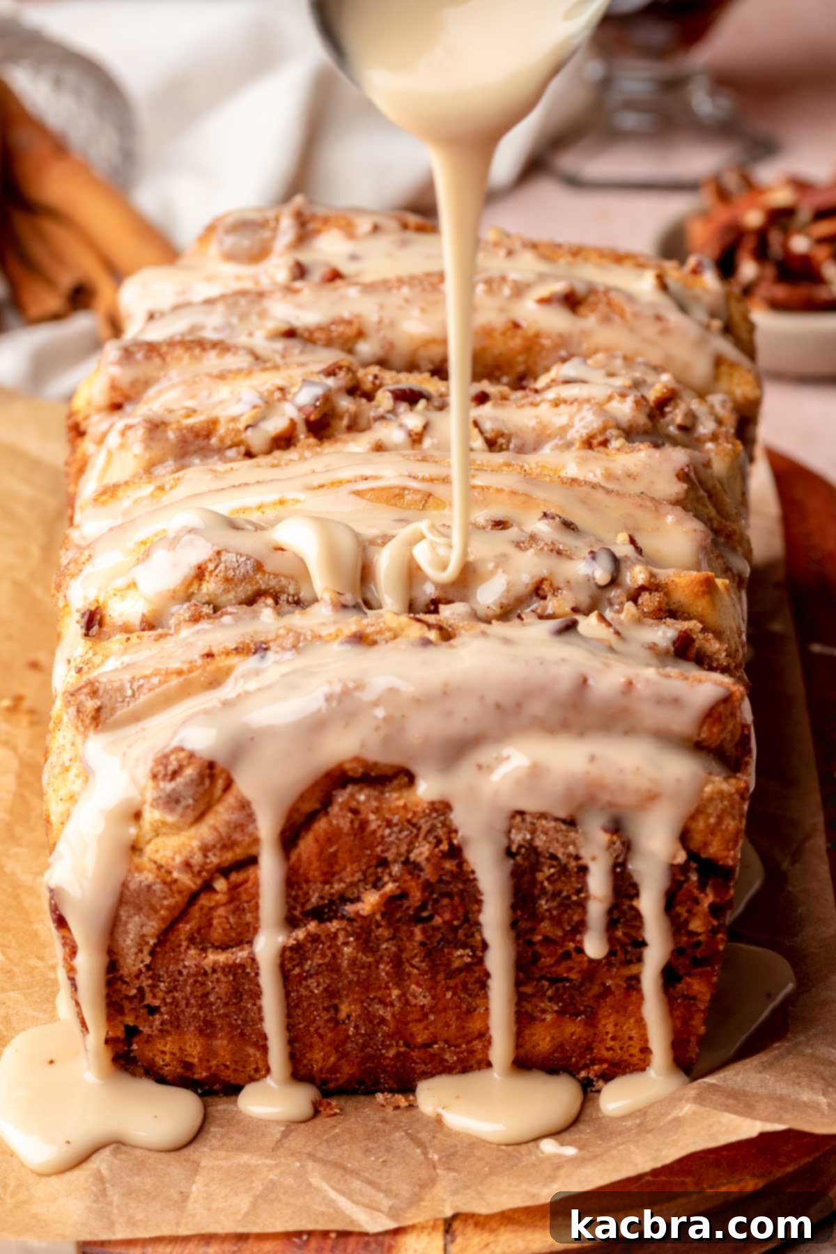 A spoon drizzling maple glaze generously over warm, freshly baked cinnamon pull apart bread.