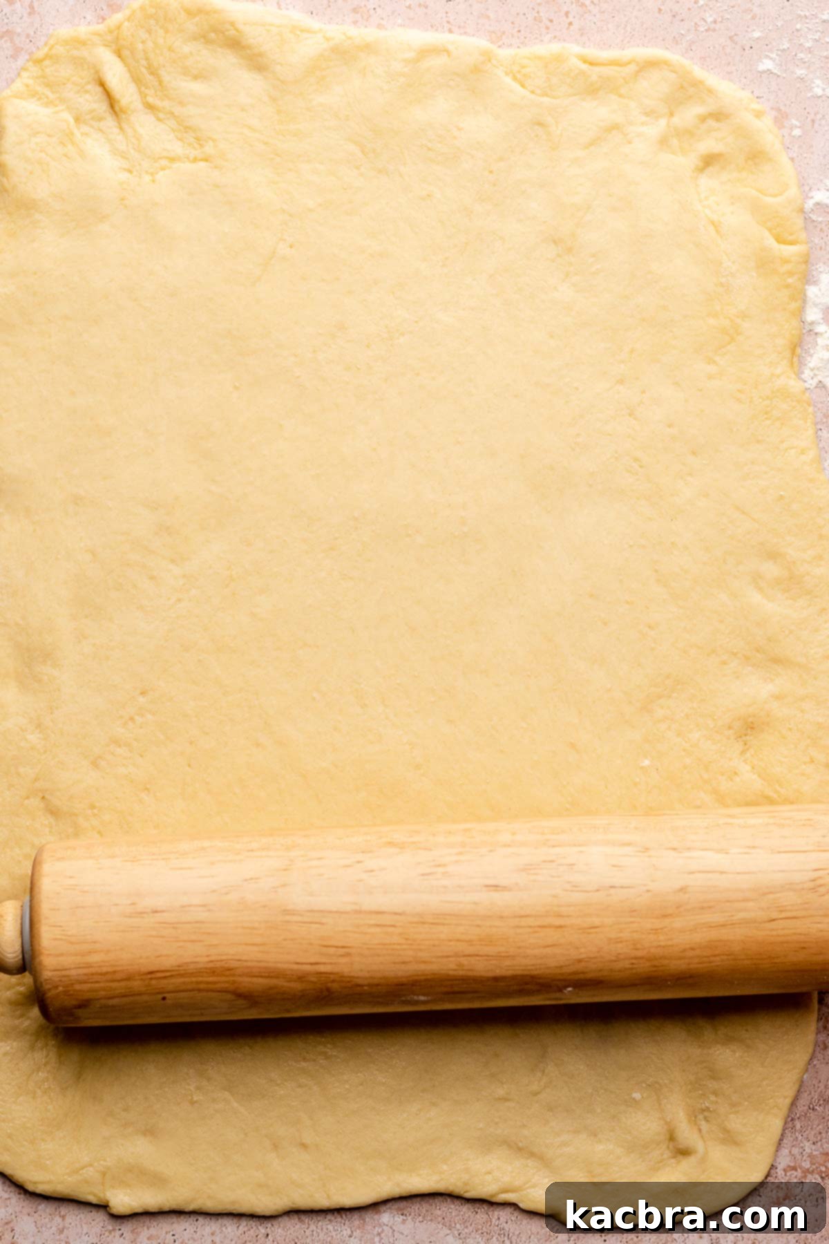 A rolling pin rolling dough into a large rectangular sheet.
