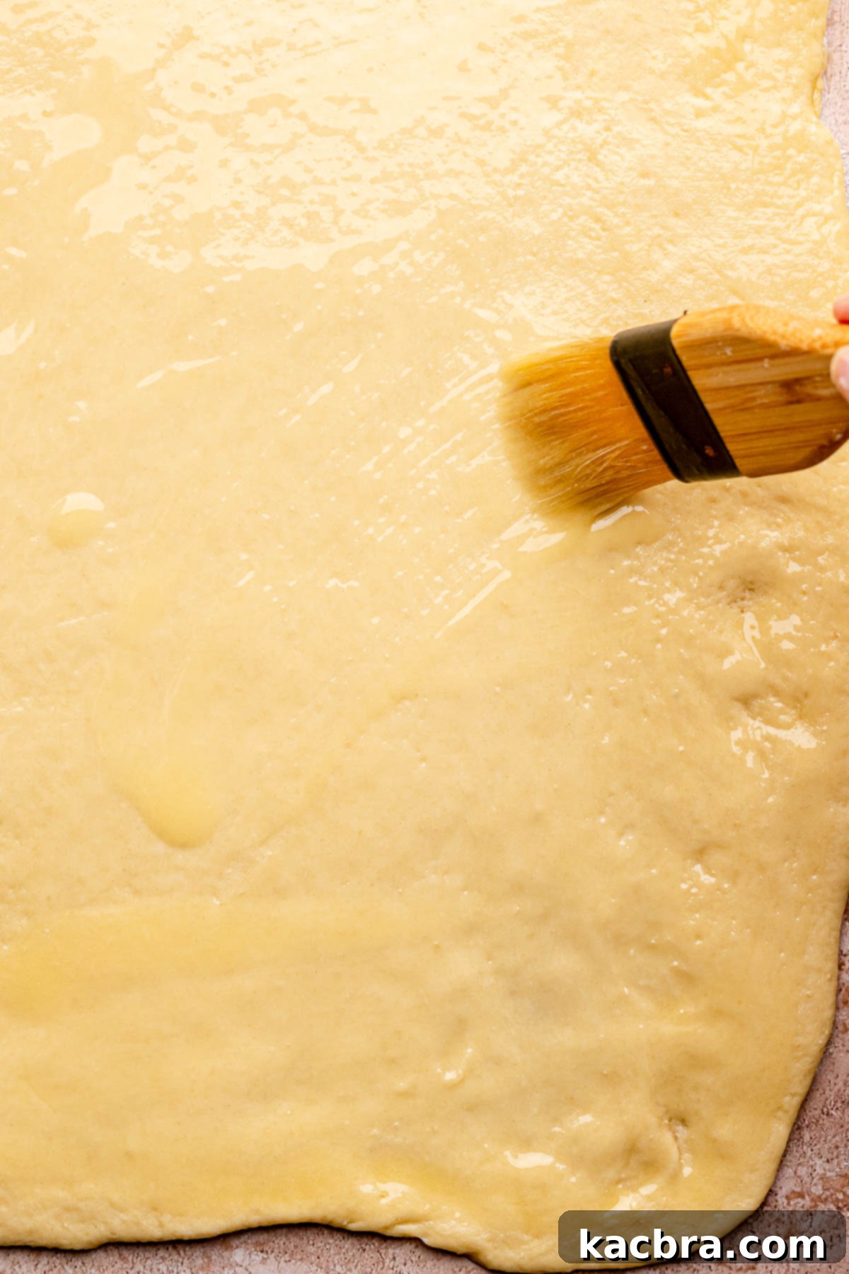 A pastry brush spreading melted butter evenly onto rolled out dough.