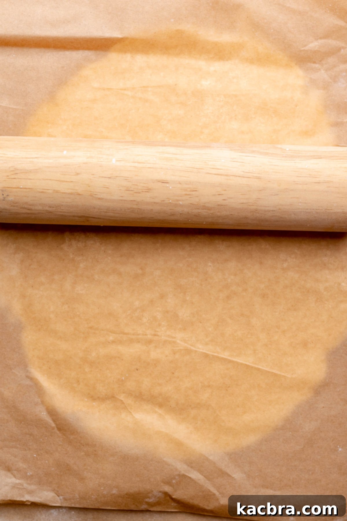 A rolling pin rolls out peppermint filling in between parchment paper.