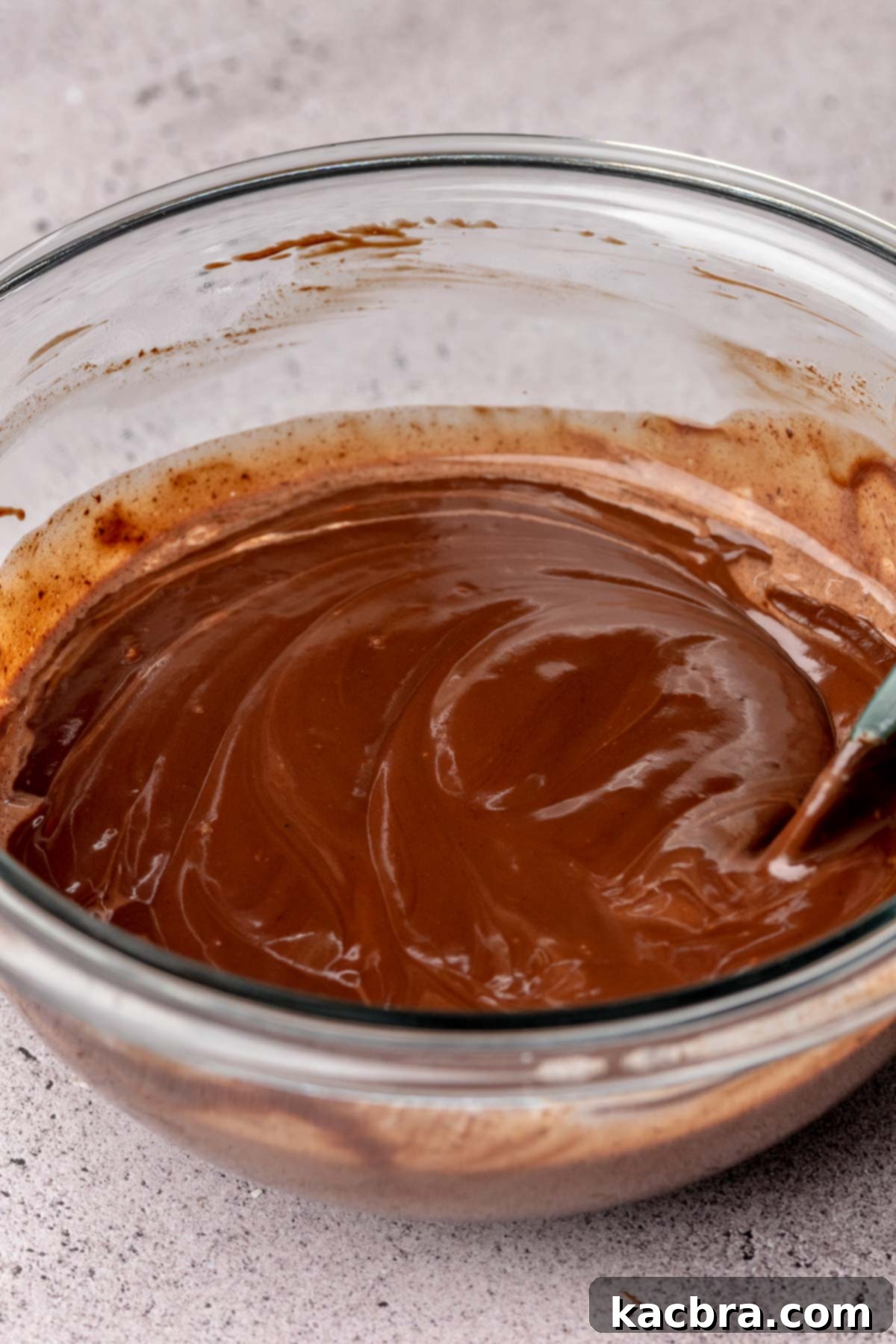 A spatula mixes chocolate ganache in a bowl.
