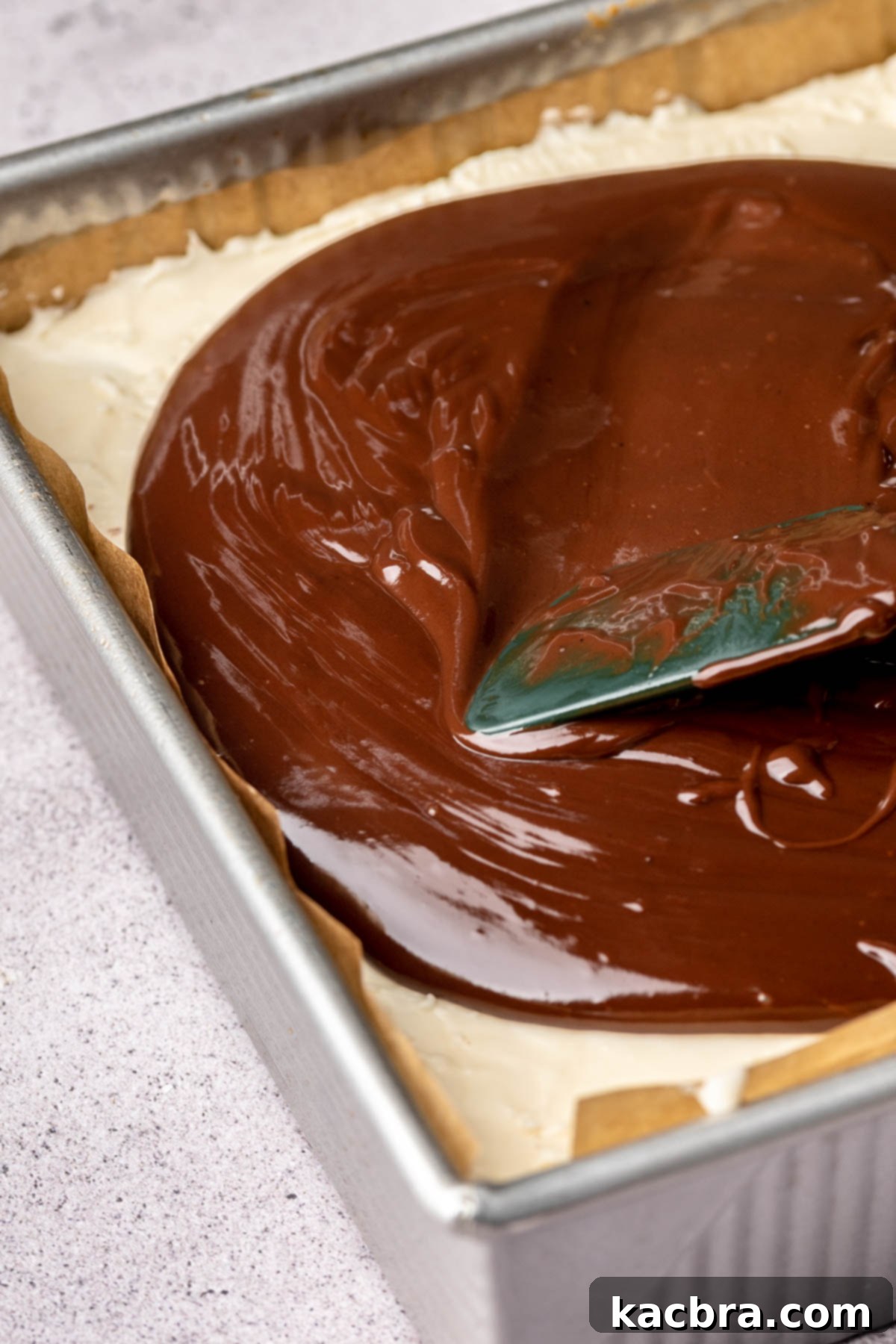 A spatula spreads chocolate ganache onto brownies.