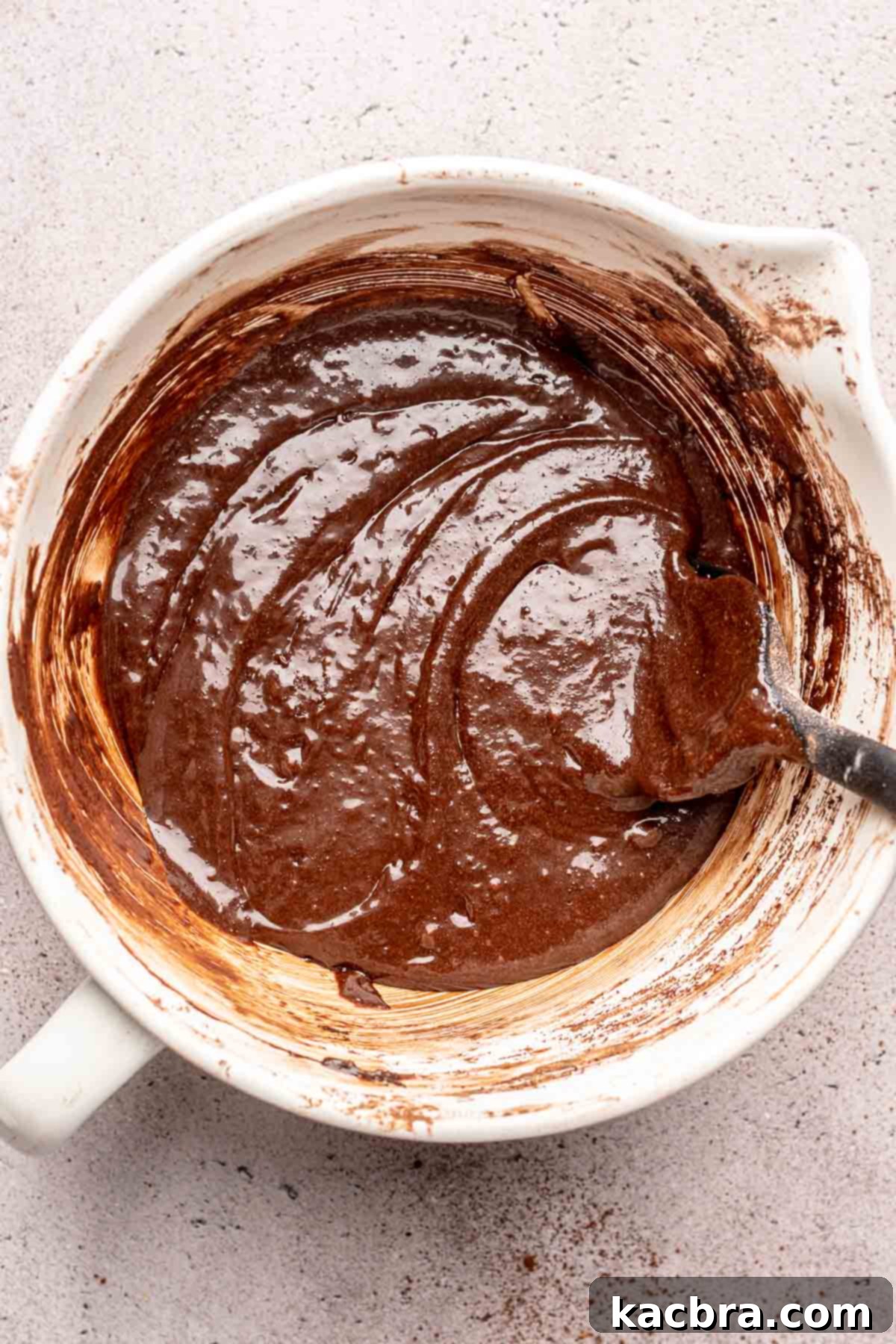 A rubber spatula mixes brownie batter in a bowl.