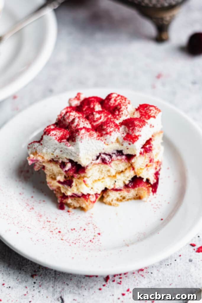 A delectable slice of cherry almond tiramisu, revealing its luscious layers, perfectly portioned on a white plate with a spoonful missing.