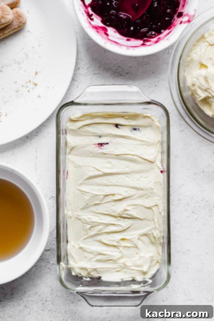 The cherry compote is spread evenly over the ladyfinger layer, creating a vibrant base.