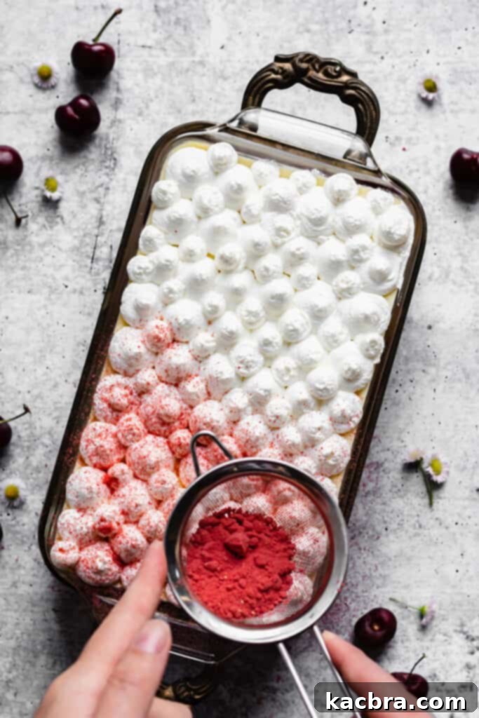 A layer of fresh whipped cream is gently piped onto the top of the tiramisu, preparing for the final dusting.