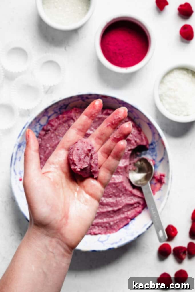 A scoop of unrolled raspberry fudge resting in the palm of a hand, prepared for shaping.