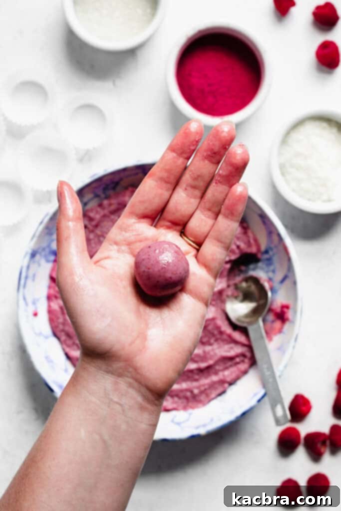 A perfectly rolled and smooth ball of raspberry fudge resting in the palm of a hand, ready for its coating.