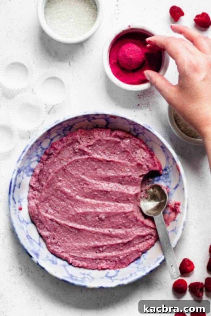 The smooth raspberry fudge ball being gently tossed and coated in bright freeze-dried raspberry powder, adding an extra layer of flavor and visual appeal.