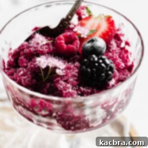 One cup of Berry Sangria Granita topped with fruit and decorative flowers. A spoon sits in the coupe.