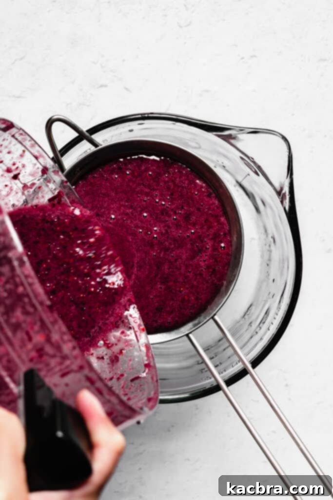 The berry puree is being poured into a fine mesh sieve.