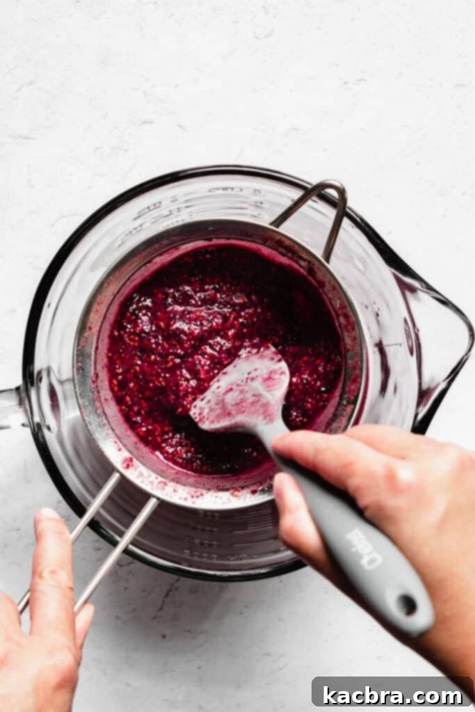 A spatula stirs the berry juice through a fine mesh sieve.