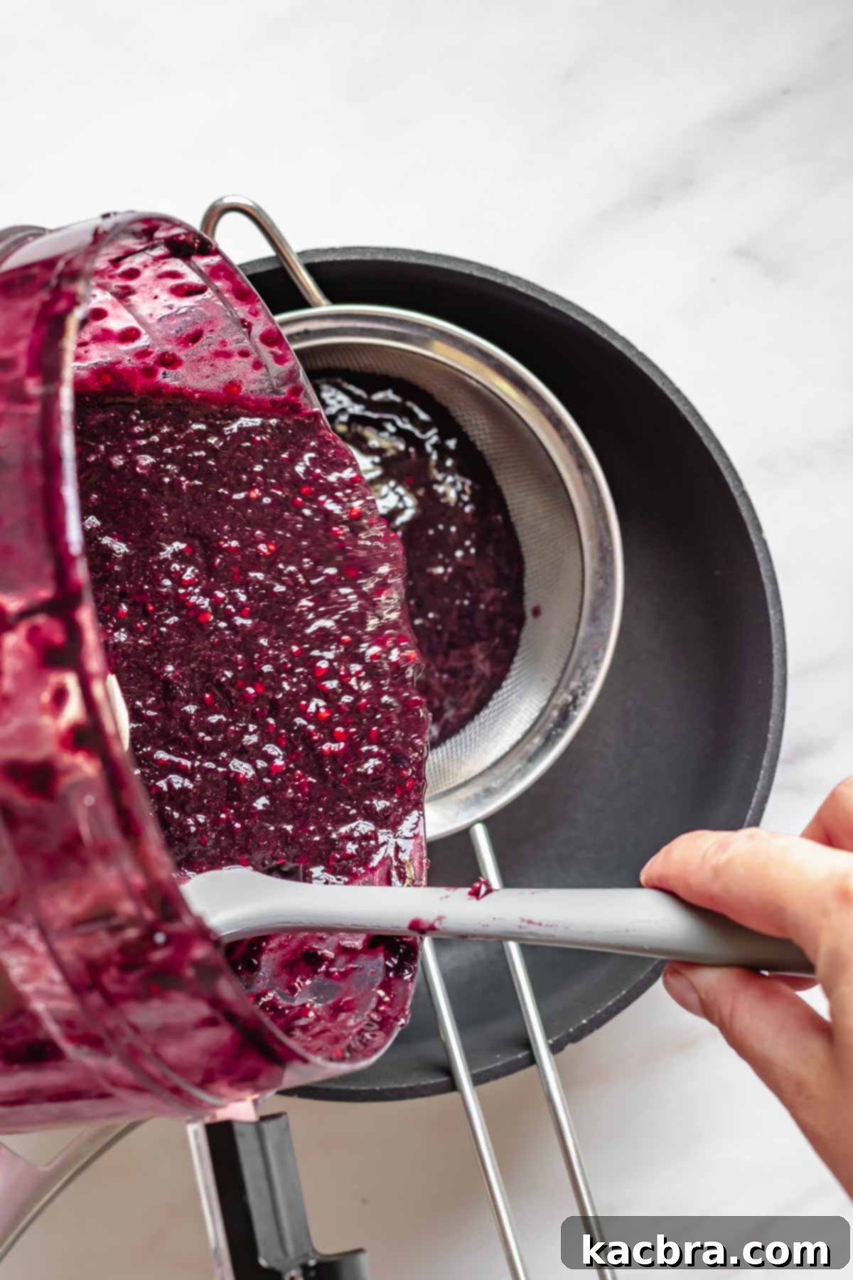 Black raspberry puree pouring into a fine mesh strainer.