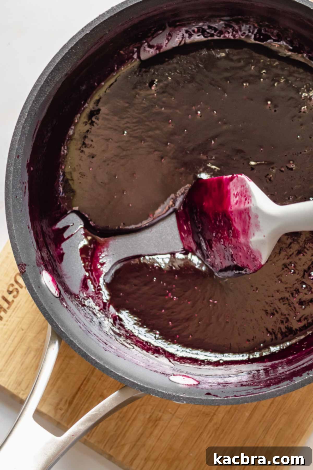 A spatula drags reduced blackberry puree in a pot.